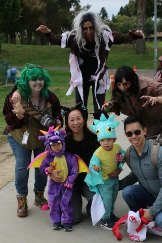 A zombie performer reaches both arms toward the camera in a striking close pose.