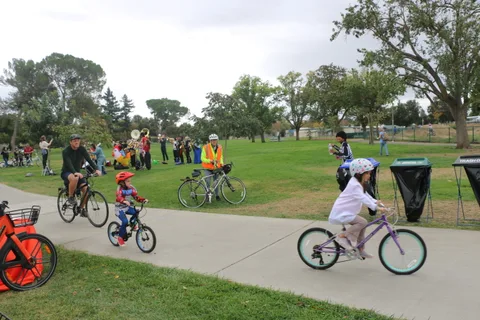 A child rides a small bike across a wide, empty stretch of park.