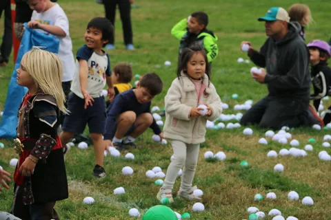Kids kneel on the grass gathering balls as a man crouches beside them.