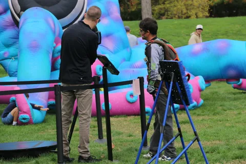 Two men stand near a target game beside a giant inflatable sculpture.