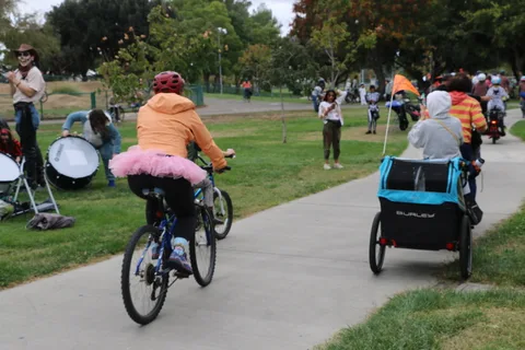 A rider in a pink tutu costume pedals away from the camera pulling a cart.