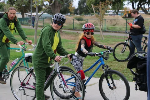 Riders in a green dinosaur costume and red zombie makeup stand with their bikes.