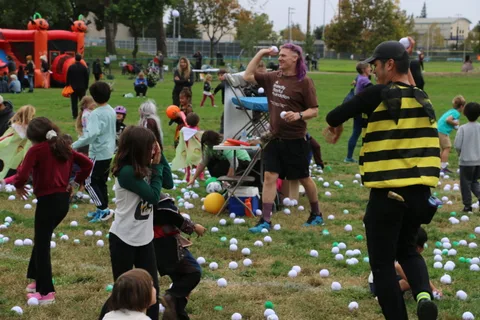A pink-haired figure reaches for a ball as kids in costume gather around.