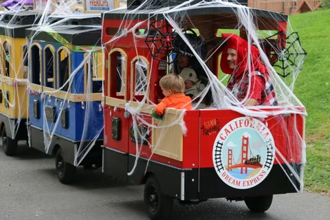 A costumed boy with red horns rides inside a cobweb-covered train car.