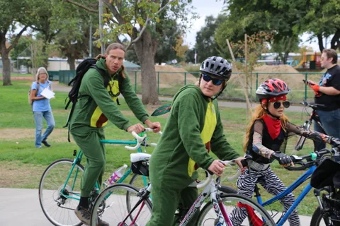 A small group in costume rides bikes away from the camera down the path.