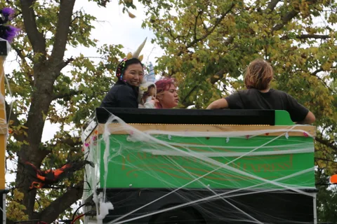 Two people sit inside a green trolley car decorated with spooky spiderwebs.
