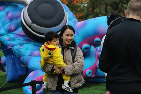 A mother carries her daughter dressed as a duck near a giant inflatable sculpture.