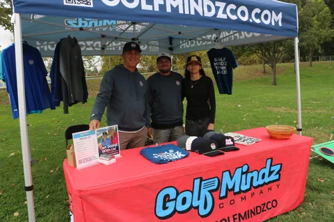 Three GolfMindz staff members smile behind their booth table at the festival.