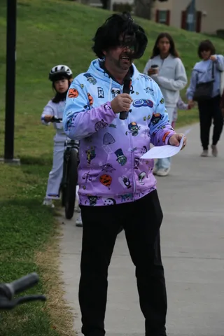 A man in a skull-patterned purple jacket and top hat walks his bike down the path.