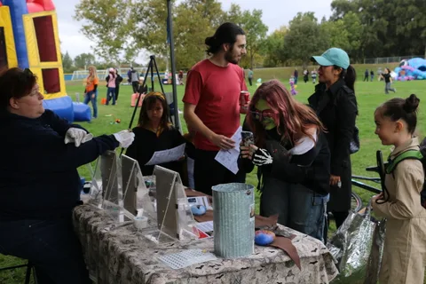 Visitors browse a booth table as a man looks on in the background.