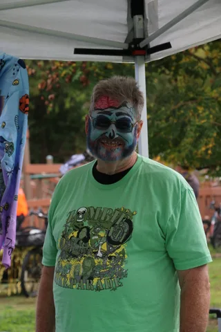 A man's face is painted with grey zombie makeup, seen from a slightly different angle.