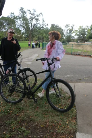 A man chats with a costumed zombie rider straddling her bike on the path.