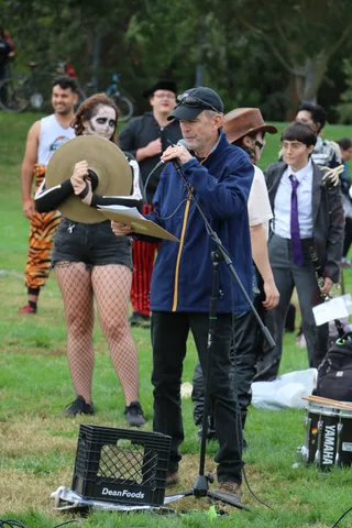 A costumed group gathers around a man singing into a microphone.