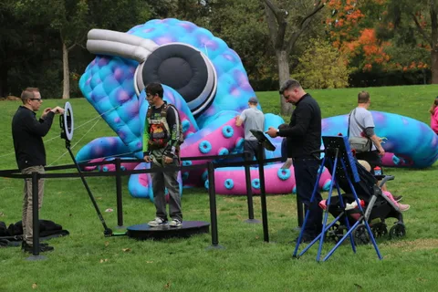 A man aims at a target in front of a giant blue and pink inflatable caterpillar.