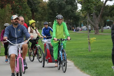 A father and two kids in bright helmets ride together, smiling toward the camera.