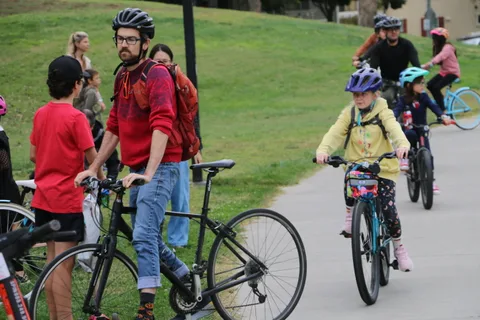 An adult and a child in a yellow helmet ride together on the path.
