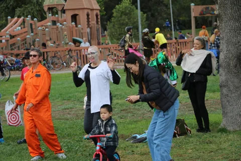 A crowd in orange jumpsuit costumes gathers near the playground.