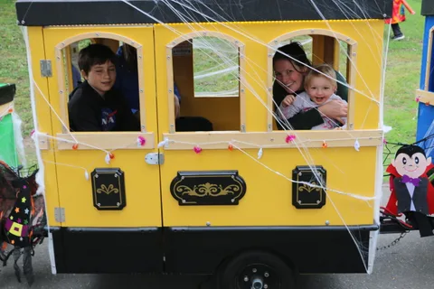 A boy waves from a train car window as a man holds a baby in the next car.