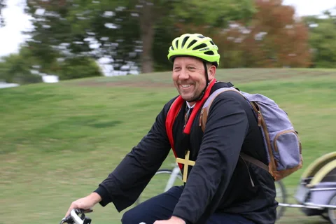 A man in priest-style costume rides away with slight motion blur.