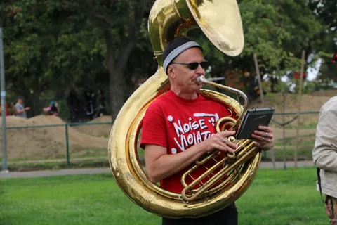 A sousaphone player in a Noise Violation shirt performs in warm light.