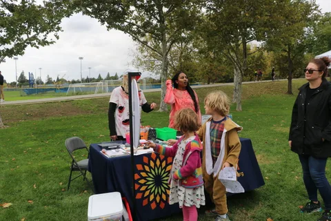 A woman and children gather near a prize wheel booth in the park.