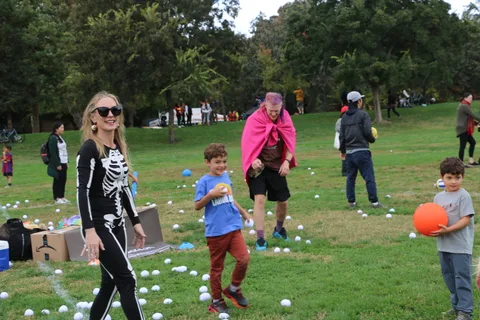 A woman in skeleton face paint and a black bodysuit stands in a grassy park.