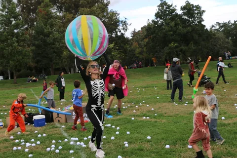 A girl in a skeleton costume reaches up for a large striped ball at the festival.
