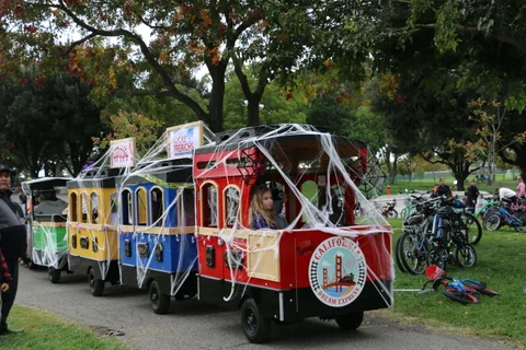 Colorful decorated train cars are parked on the path with riders gathering behind.