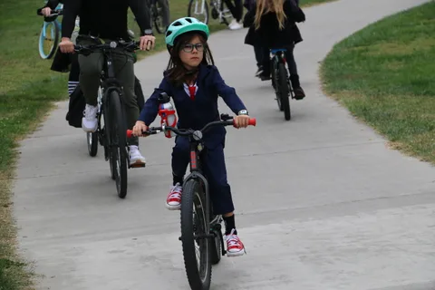 An adult and a girl in blue ride bikes close together on the path.