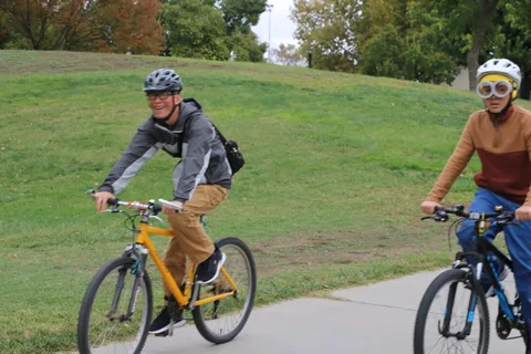 A man in an orange and black jacket rides alone on the path.