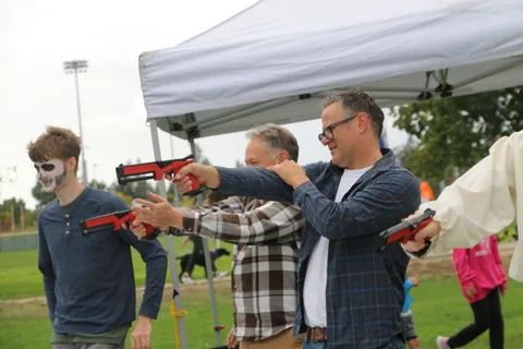 A teenager and an older man aim red toy blasters at each other under a tent.