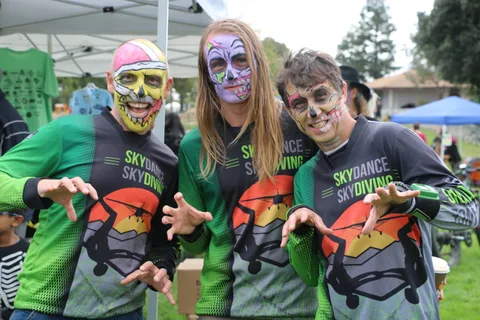 Three people in Skydance Skydiving shirts pose with skull face paint at the festival.