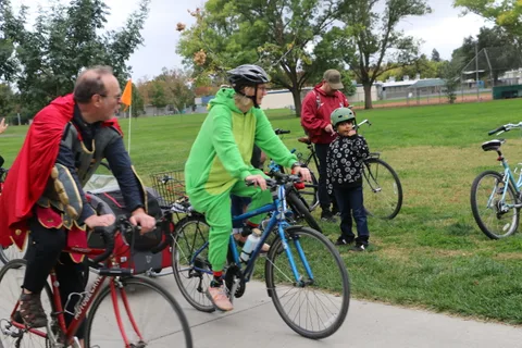 A man in a dark jacket rides past a colorfully costumed crowd.