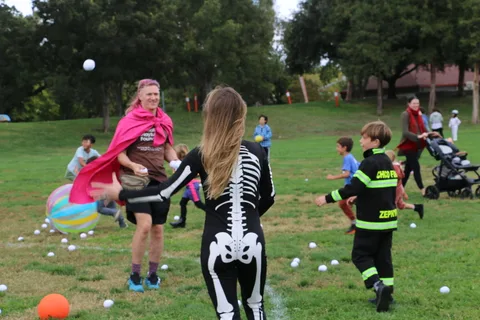 A woman in a pink cape and a child in a skeleton costume stand together, seen from the side.