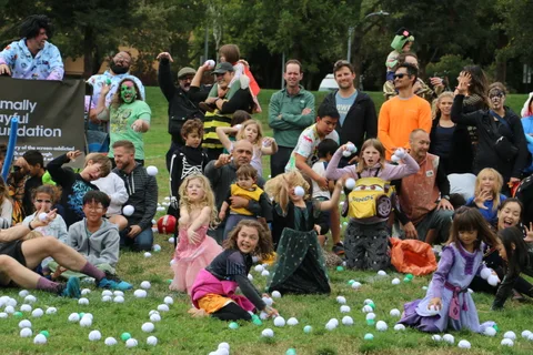 Skeleton-costumed figures stand among a crowd of festival-goers on the grass.