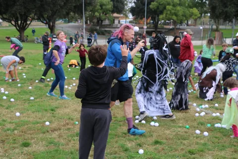 A boy and an adult scoop up balls as a ghost-costumed figure moves past in a blur.