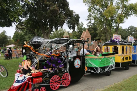 Halloween-decorated trackless train cars sit parked along a park path.