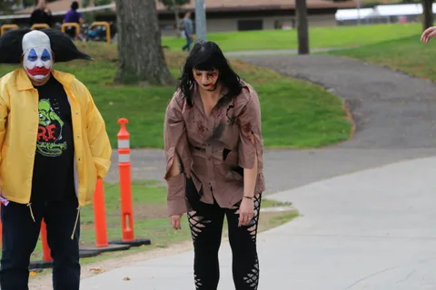 A zombie performer with red makeup strides across the grass.
