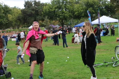 A man in a pink cape reaches playfully toward a child at the festival.