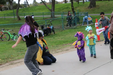 A costumed woman crouches to greet a child dressed as a dragon.