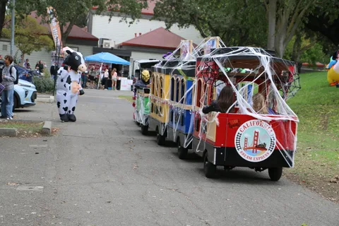A row of decorated train cars sits parked with a cow-costumed figure in the distance.