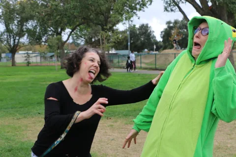 A woman and a person in a green frog costume share a laugh in the park.