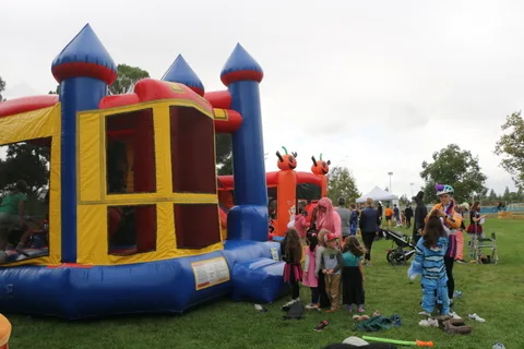A bounce house castle stands in a park with children and parked bikes nearby.