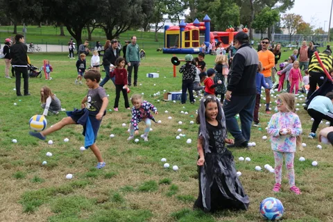 A boy kicks a ball near the bounce house as other kids play nearby.