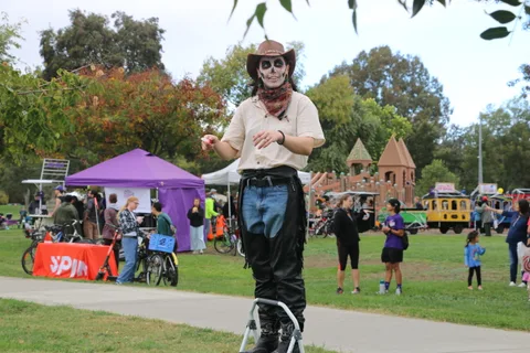 A man in skeleton face paint walks while holding a drumstick.