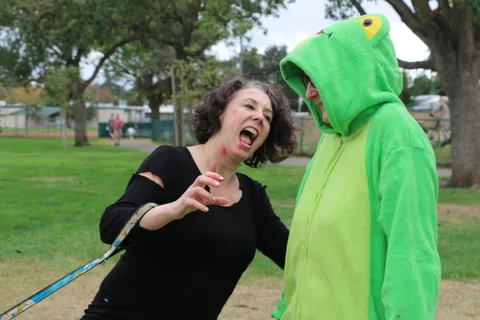 A woman calls out while a person in a green frog costume covers their face.