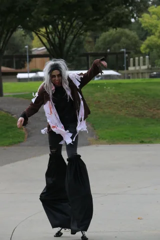 A performer in zombie makeup and tattered costume moves along the path.