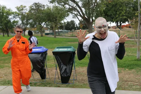 A person in a bald-cap zombie costume reaches playfully toward the camera.