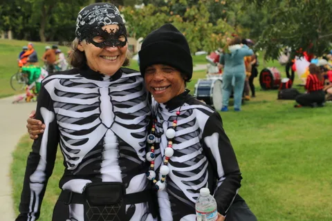 A skeleton-costumed adult and child pose smiling together in the park.