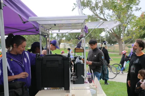 A man in the foreground stands near a purple booth as another man gestures behind him.